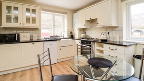 Een moderne keuken met witte kasten, een glazen eettafel en een zwarte stoel.