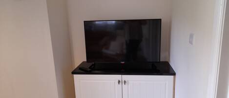 A room with a flat-screen TV on a black stand, a remote control, and a white cabinet with two doors.