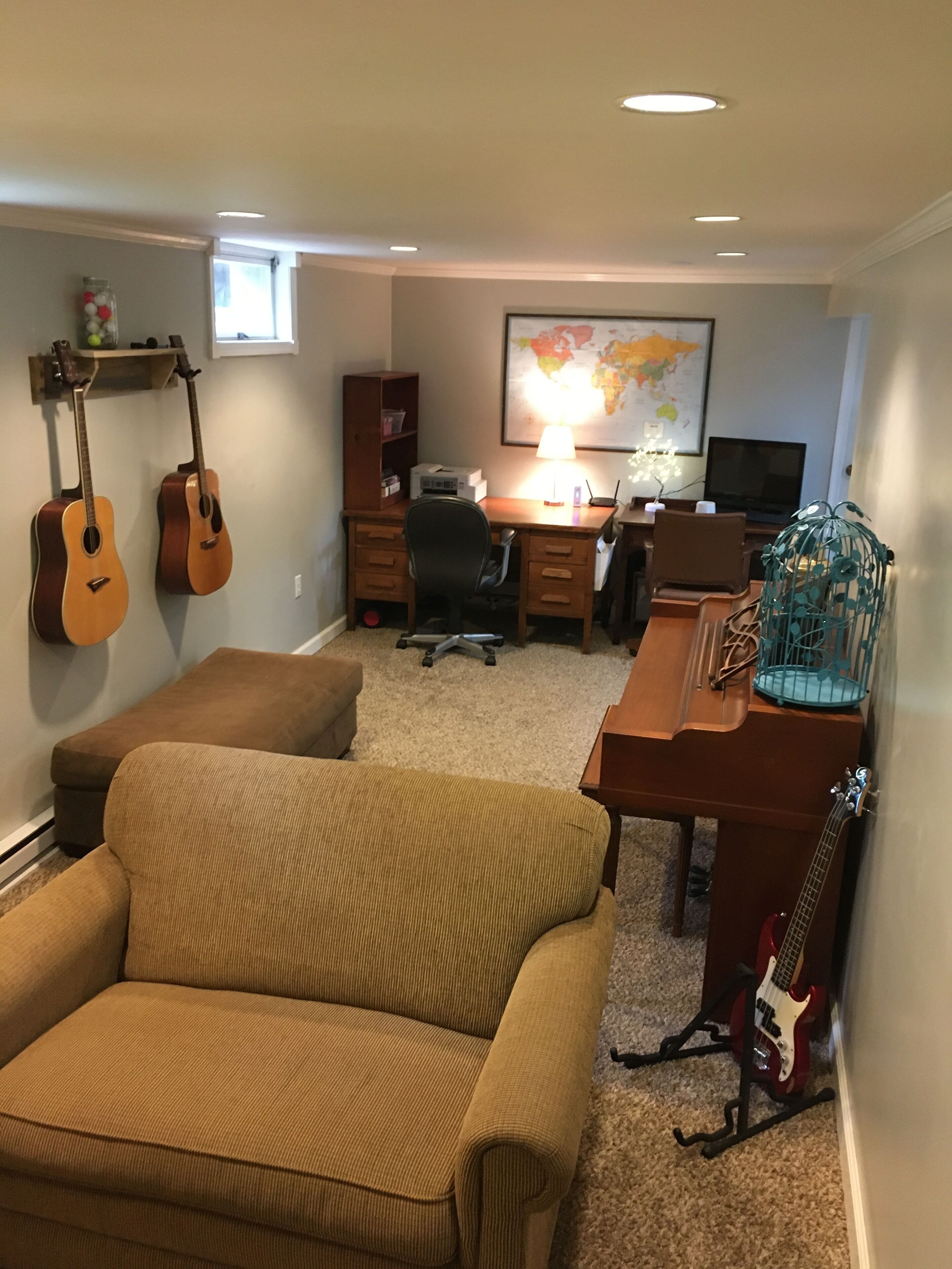 A cozy room with a brown sofa, a wooden desk with a computer, a guitar, and a bookshelf.