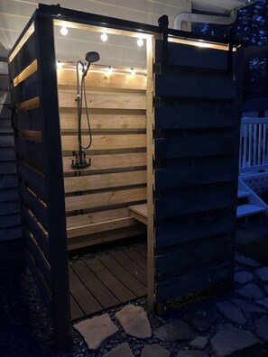 A wooden sauna structure with a bench inside, a showerhead, and a hose.