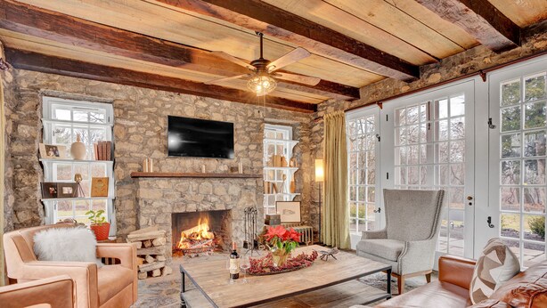 A cozy living room with stone walls, a fireplace, leather furniture, and a large window.