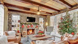 A cozy living room with leather sofas, a fireplace, a Christmas tree, and stone walls.