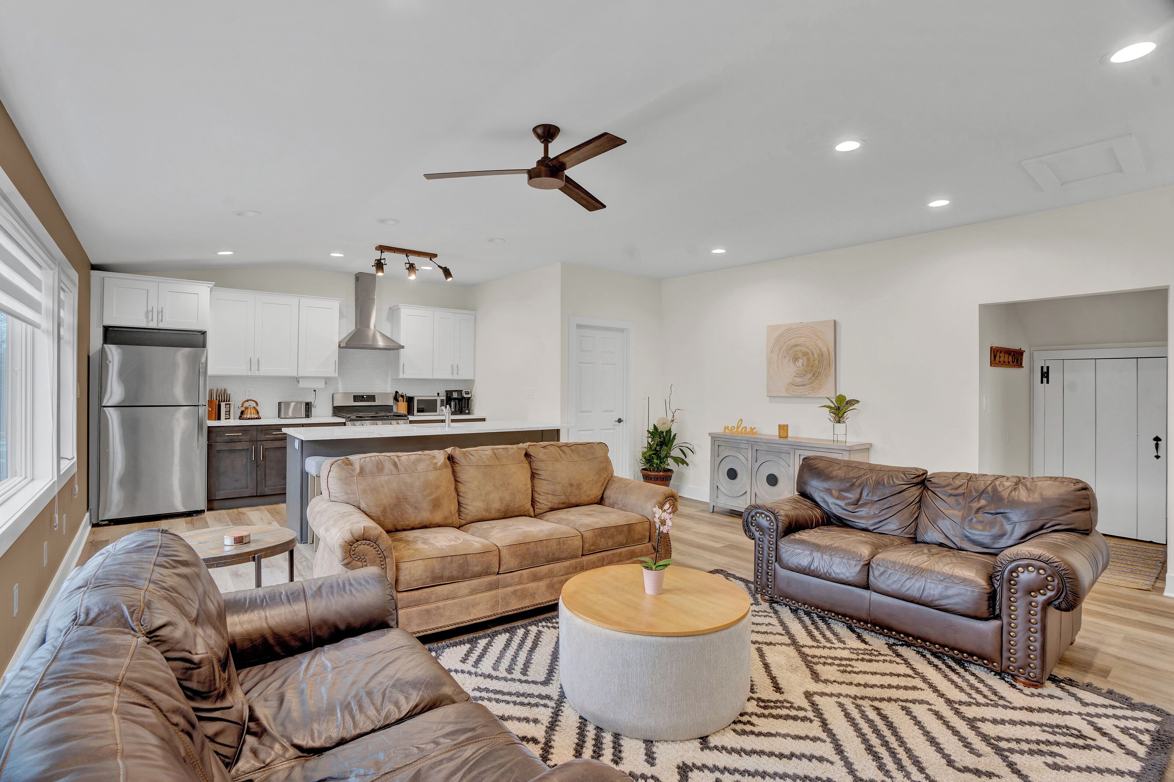 A modern living room with leather sofas, a wooden coffee table, and a kitchen in the background.