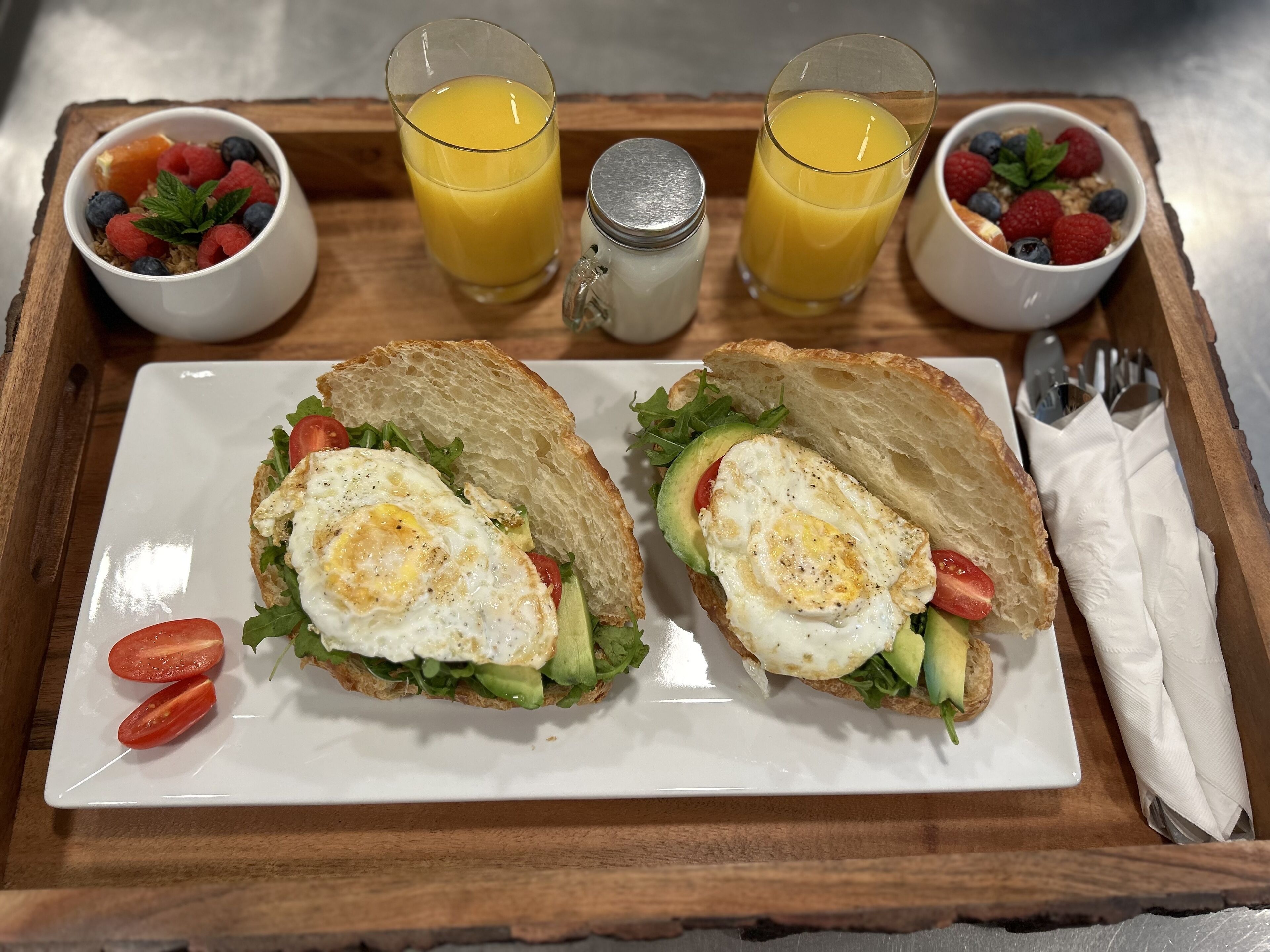 Una bandeja de desayuno con dos sándwiches, dos vasos de zumo de naranja y dos ensaladas de frutas.