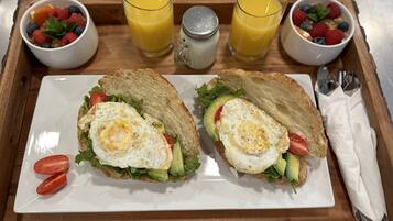 Una bandeja de desayuno con dos sándwiches, dos vasos de zumo de naranja y dos ensaladas de frutas.
