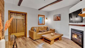 Un salon doté d’un plancher en bois, d’un canapé en cuir, d’une table basse en verre, d’une cheminée et d’un téléviseur fixé au-dessus de celle-ci.