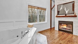 A modern bathroom with a large bathtub, a fireplace, and a large window with a view of trees.