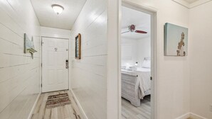 Ein Flur mit weißen Wänden und Holzböden, der zu einem Schlafzimmer mit Bett und Deckenventilator führt.