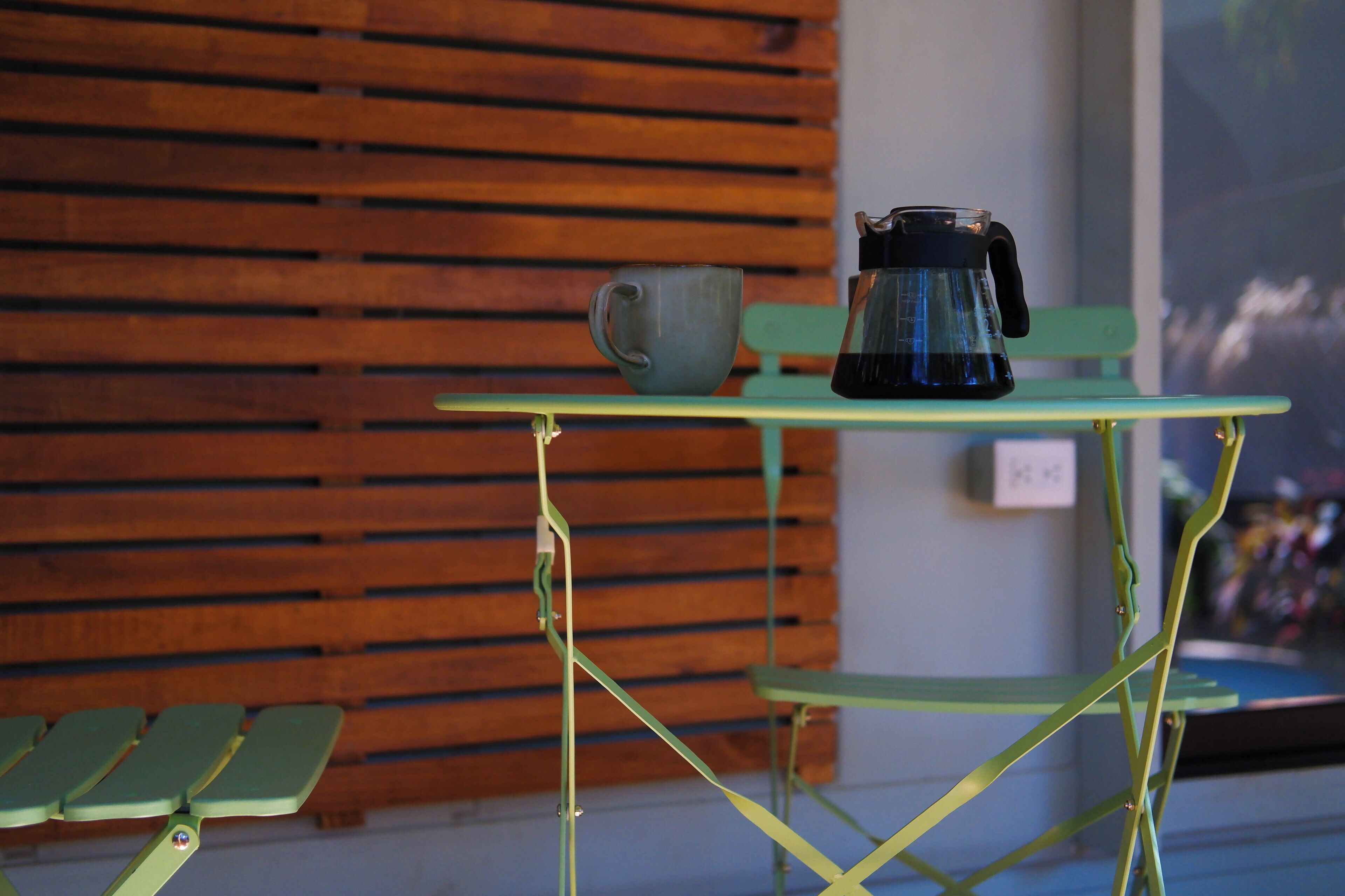 Een groene metalen tafel met een koffiezetapparaat en een mok erop.