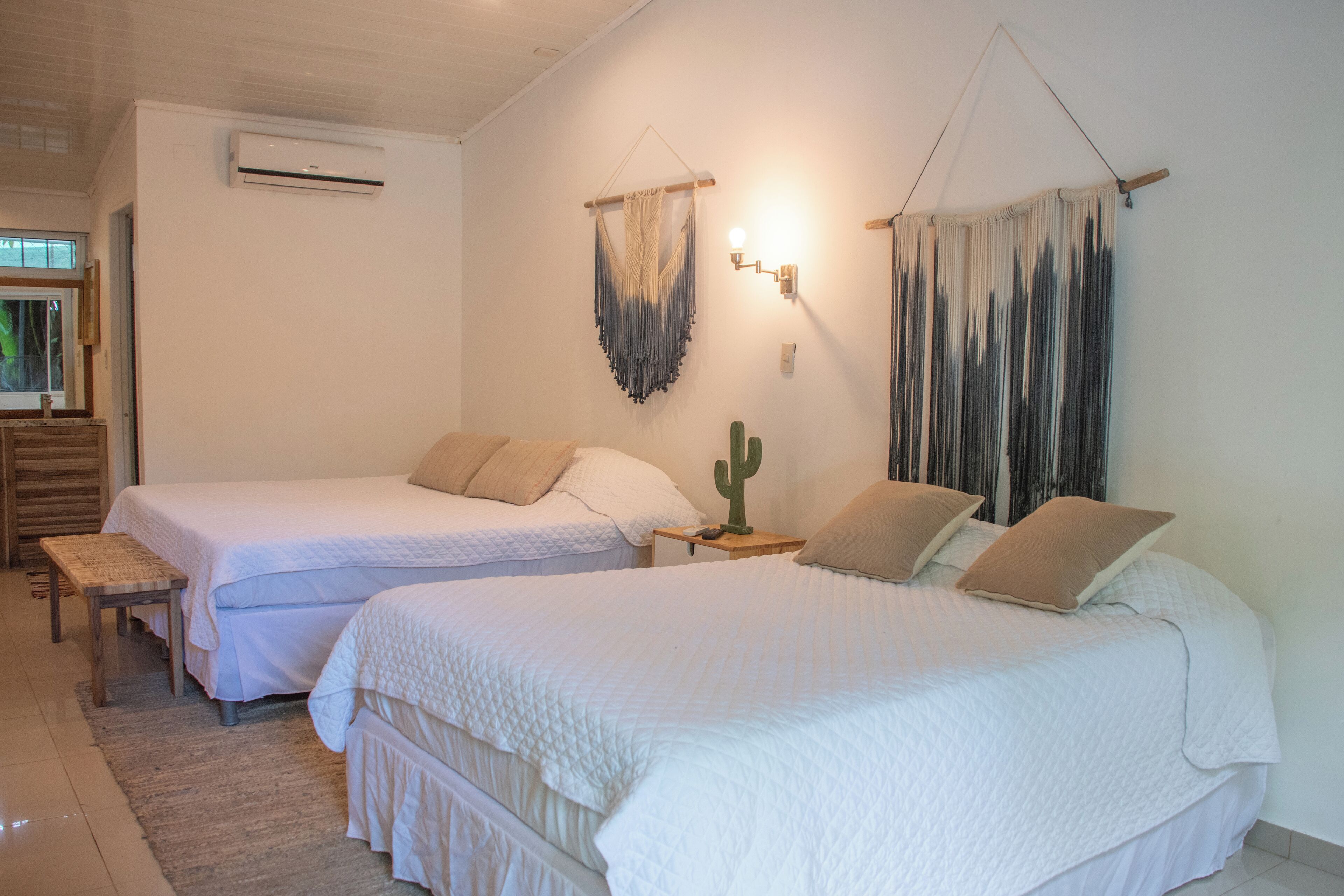 A bedroom with two beds, a cactus decoration, and a wall-mounted air conditioner.