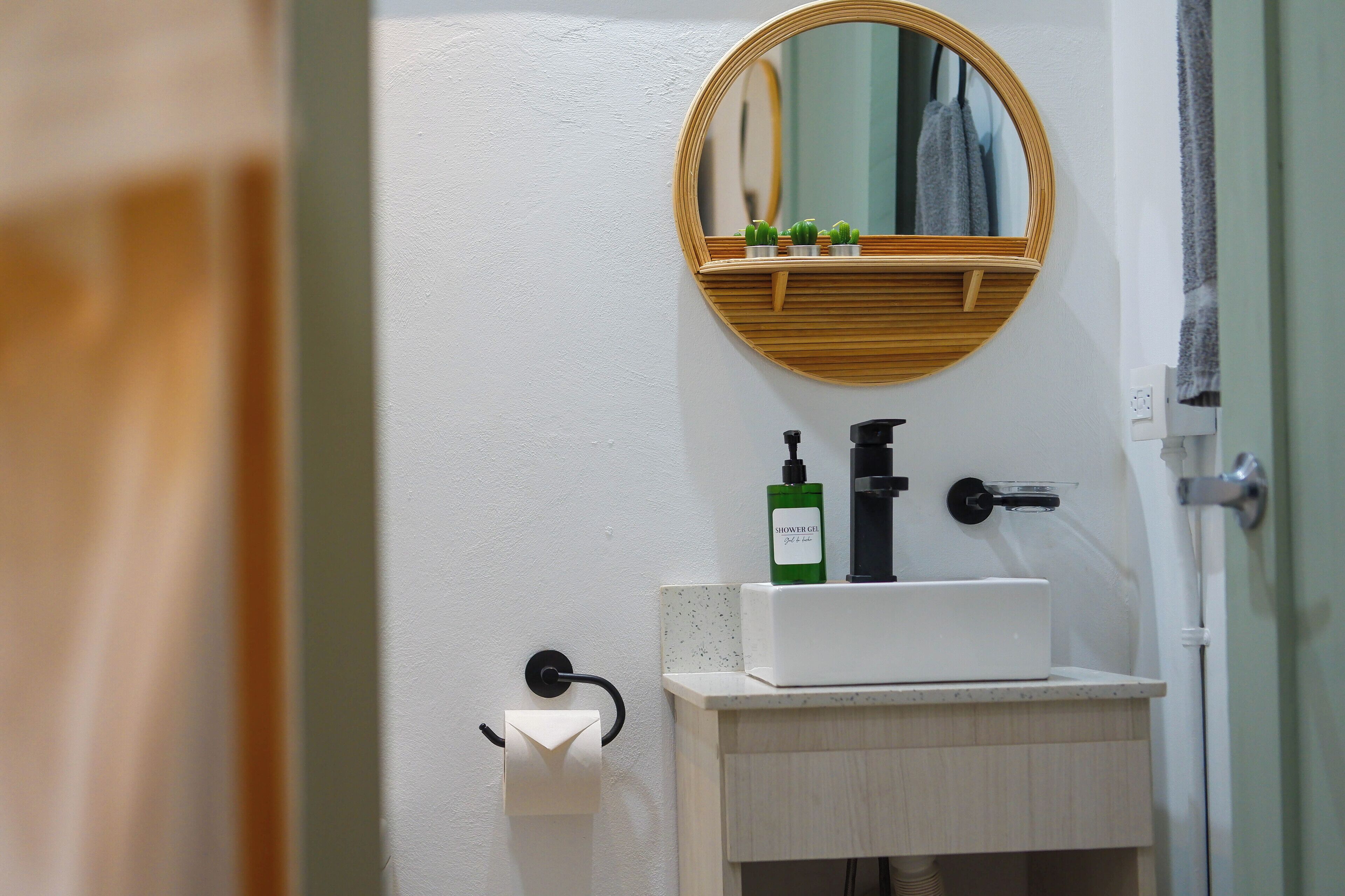A bathroom with a round mirror, a wooden shelf with toiletries, a white sink, and a towel rack.