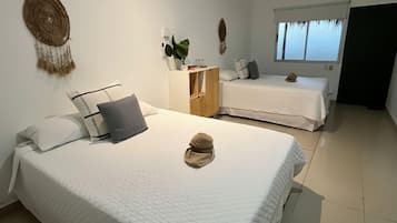 A hotel room with two beds, a ceiling fan, a dreamcatcher, a small plant, and a window with curtains.