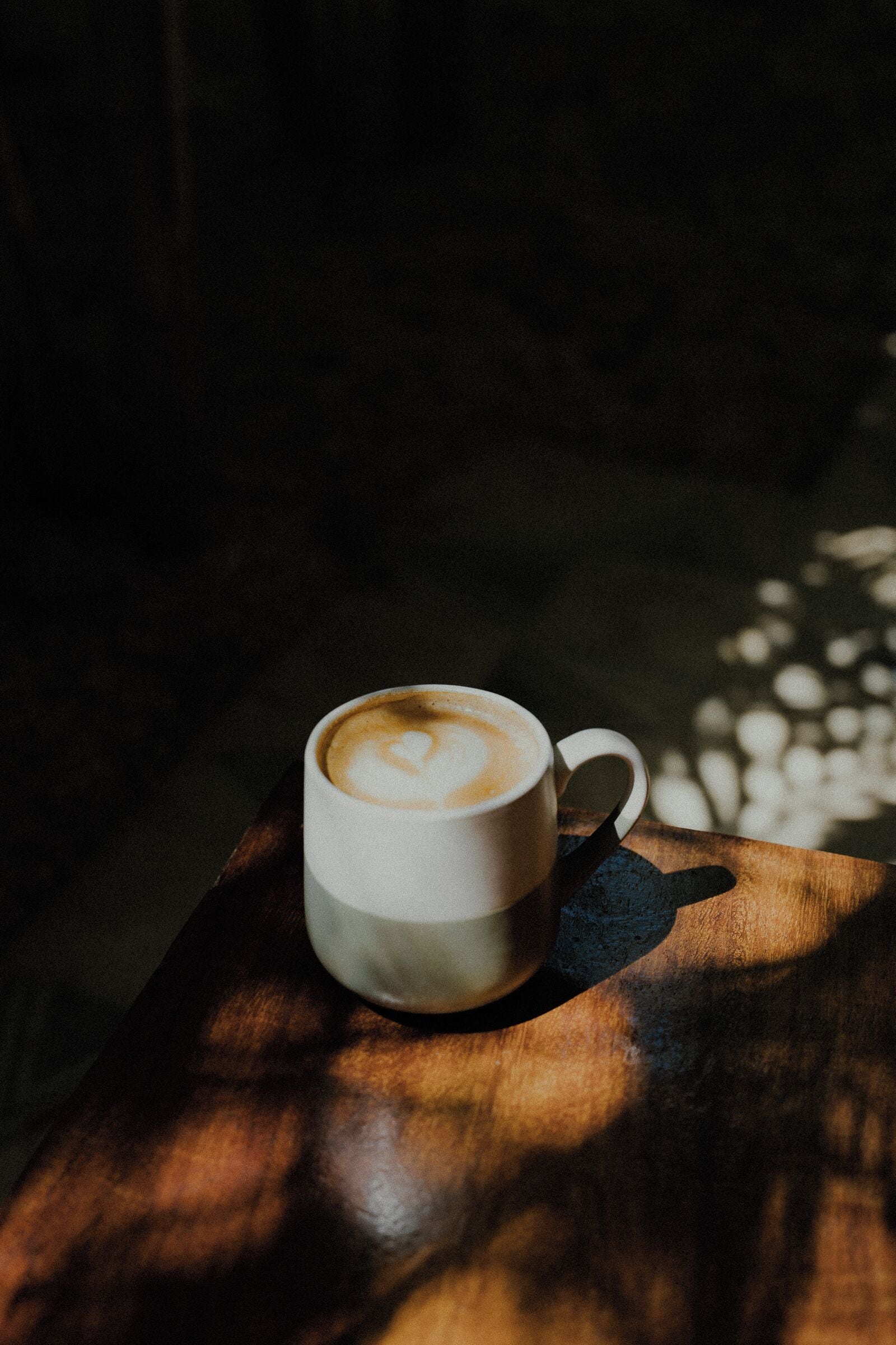 A cup of coffee on a wooden table with a shadow cast on it.