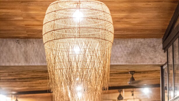 A restaurant with a large woven light fixture hanging from the ceiling, wooden walls, and a crowd of people dining. - Refugio Lodge (Tamarindo)