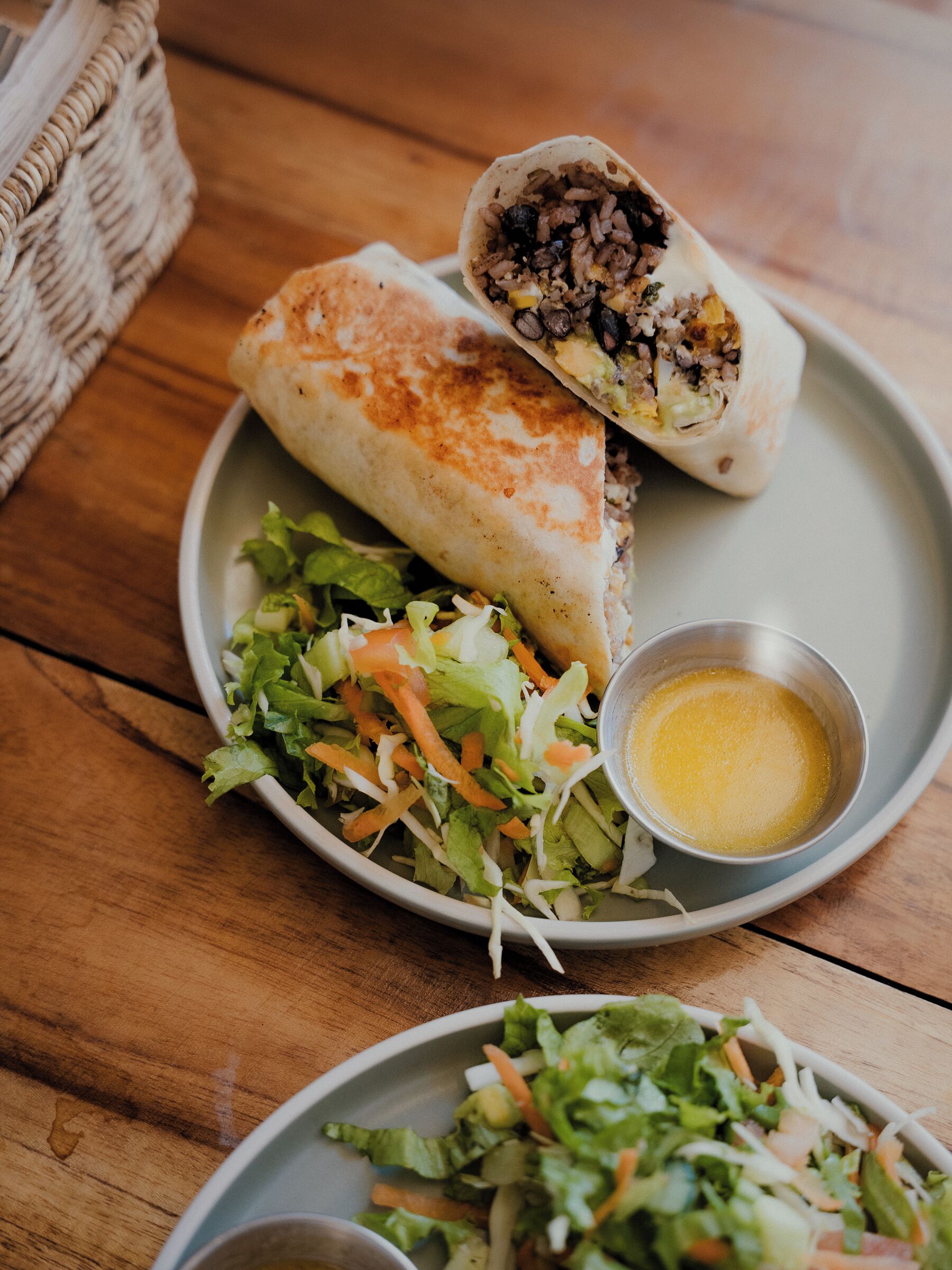 A plate with a wrap, a side salad, and a small bowl of sauce.