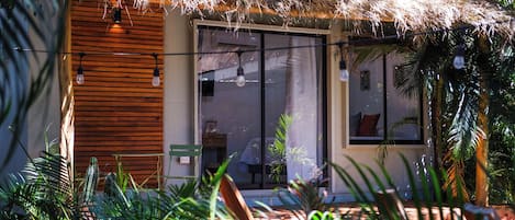 A modern house with a thatched roof, large windows, and a garden with tropical plants.