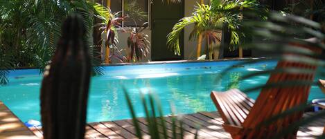 A pool area with a wooden deck, lounge chairs, and tropical plants.