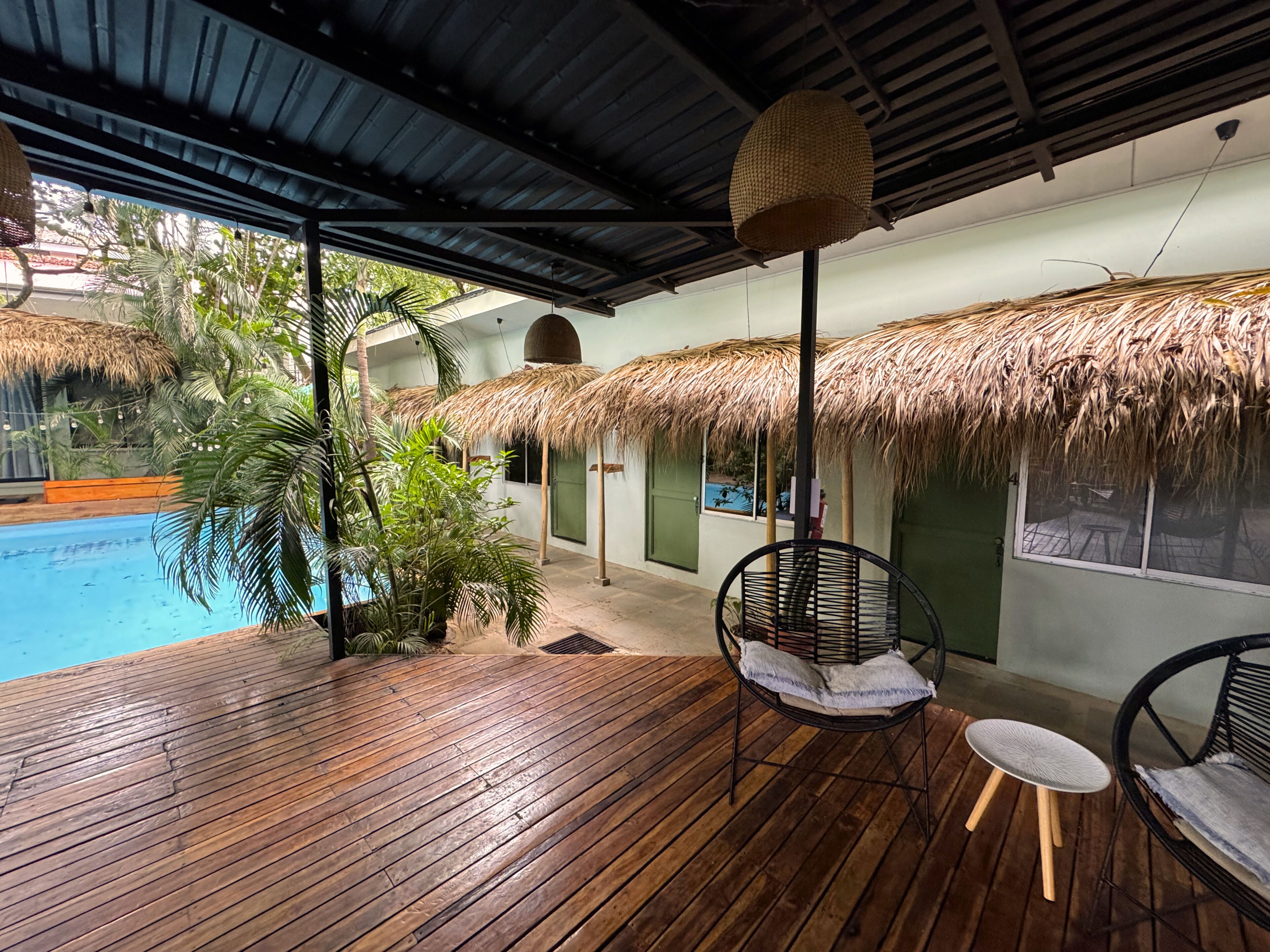 A wooden deck with a pool, thatched-roof structures, and wicker furniture.