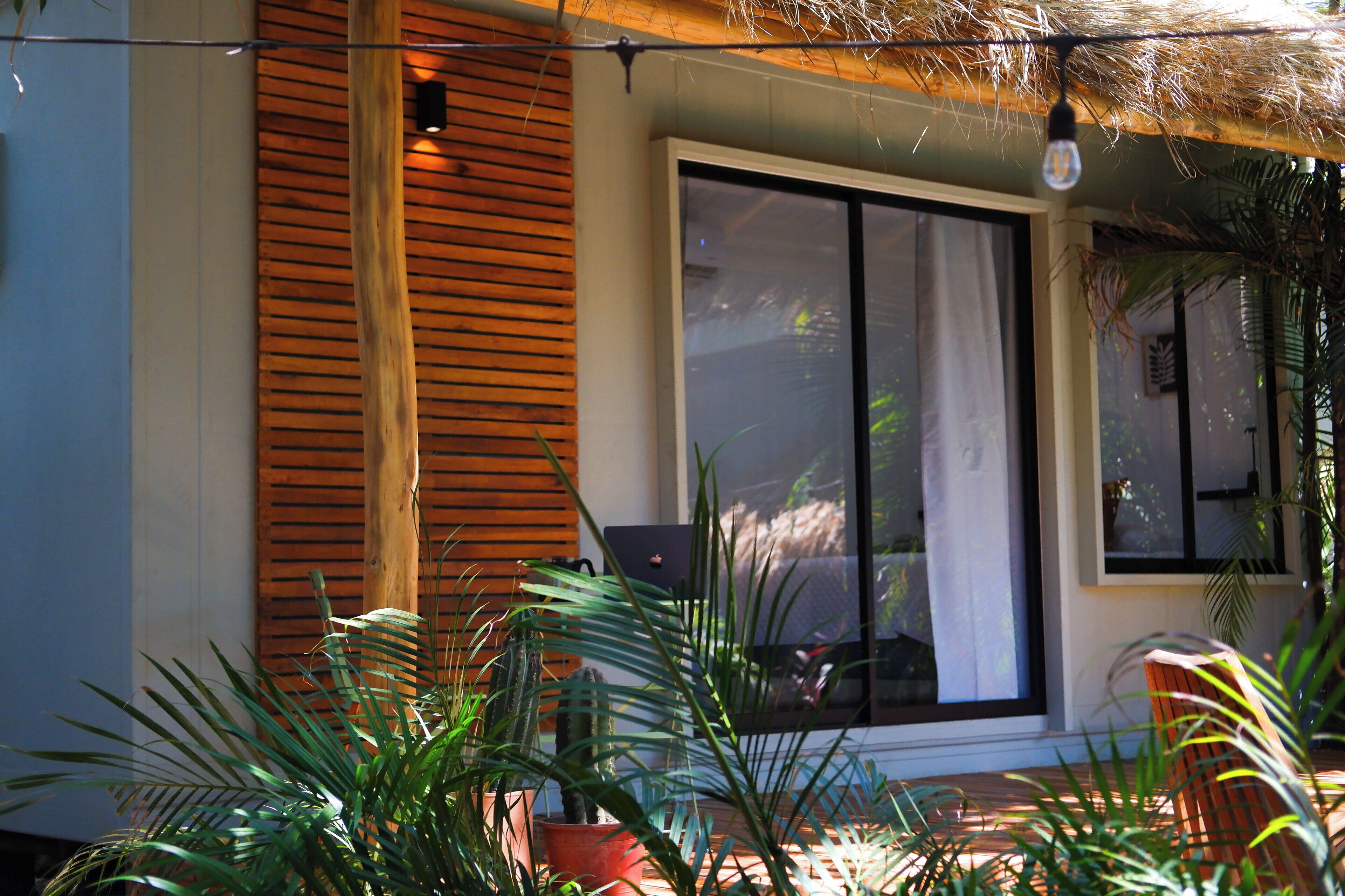 Una casa moderna con un ventanal grande, contraventanas de madera y plantas en macetas.