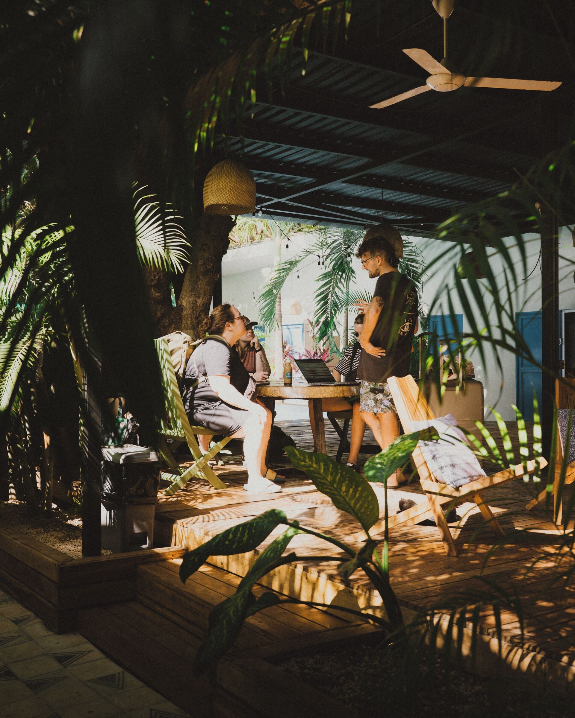 Une terrasse en bois dotée d’un ventilateur de plafond, entourée de plantes tropicales.