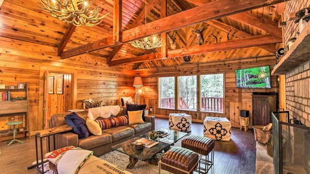 A cozy log cabin interior with a wooden ceiling, a fireplace, a comfortable seating area, and a television. - 1 Mi to Rainbow Lake: Lakeside Cabin w/ Deck! (Lakeside)