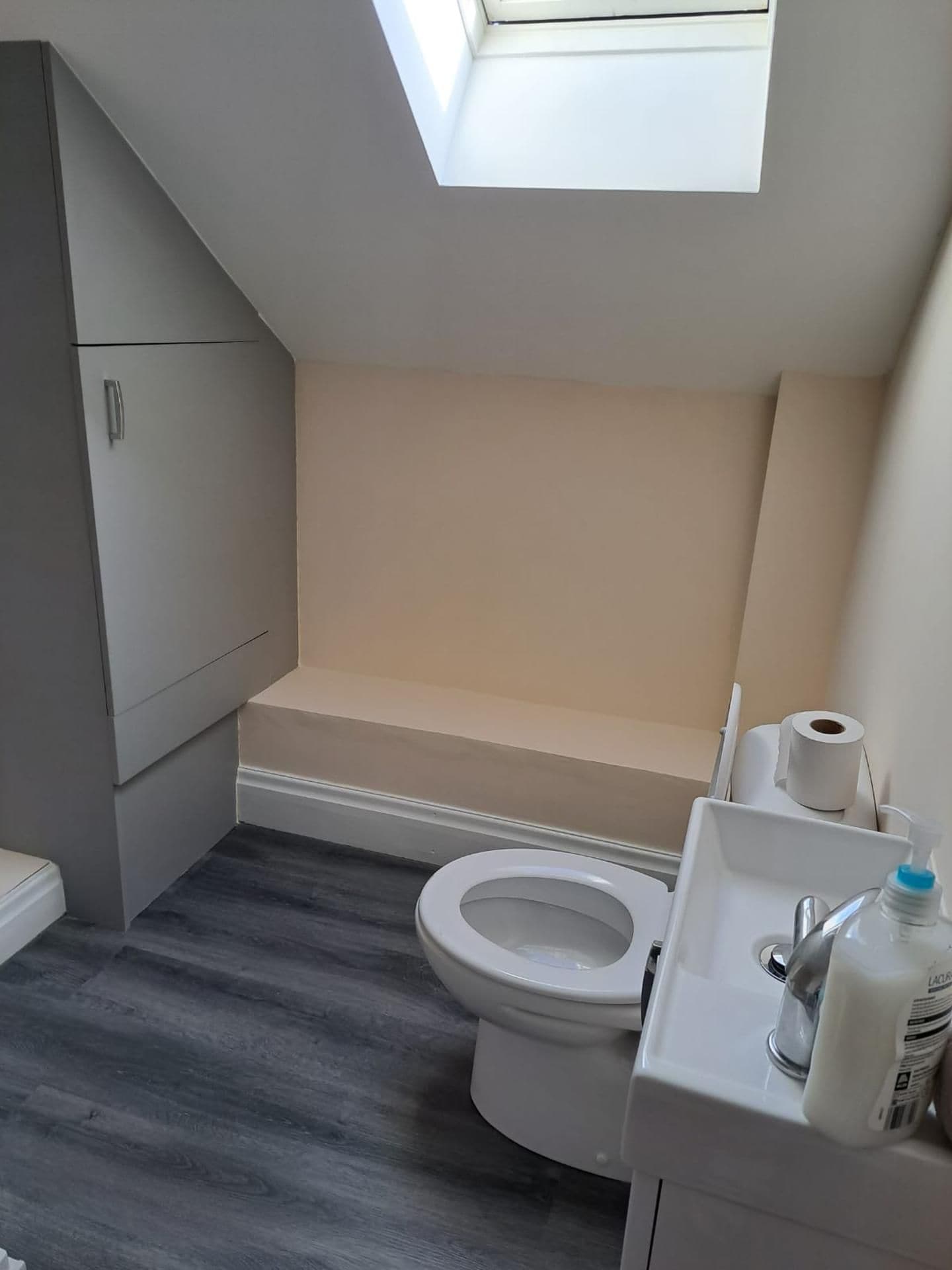 A compact bathroom with a skylight, a toilet, a sink with a soap dispenser, and a toilet paper roll.