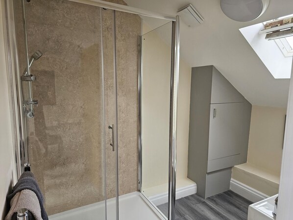 A modern bathroom with a glass shower enclosure, a white bathtub, and a grey vanity with a mirror.