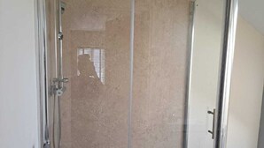 Eine gläserne Dusche mit einer weißen Badewanne, beige Wände und einem Handtuch, das an der Tür hängt.