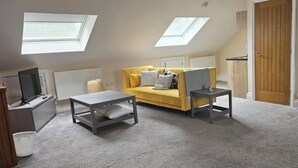 Ein Schlafzimmer im Loft-Stil mit einer Schlafcouch, zwei Sesseln, einem Fernseher und Dachfenstern.