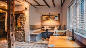 Ein gemütlicher Innenraum mit einer Steinwand, Holzbalken, einer Sitzecke mit Kissen und einem Tisch mit einer Speisekarte.