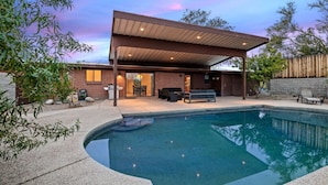 Une maison moderne dotée d’un patio couvert, d’une piscine et de mobilier d’extérieur.