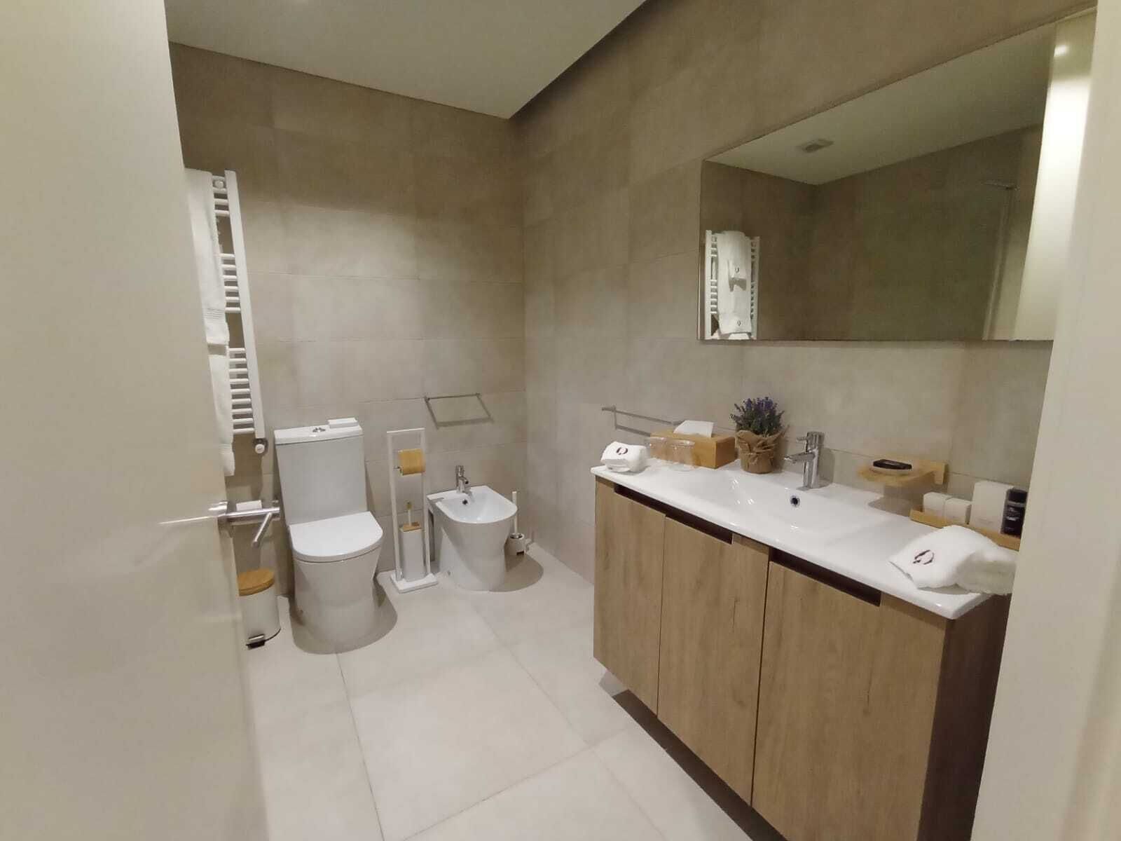 A modern bathroom with a toilet, bidet, sink, and mirror.