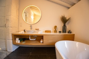 A modern bathroom with a white bathtub, a wooden vanity with a round mirror, and a vase with dried plants. - Quinta da Corredoura Hotel Rural (Guimarães)