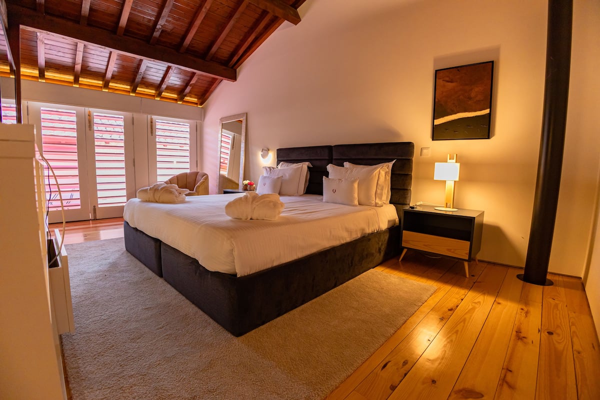 Quarto com uma cama grande, piso de madeira, mesa de cabeceira com abajur e um quadro na parede.