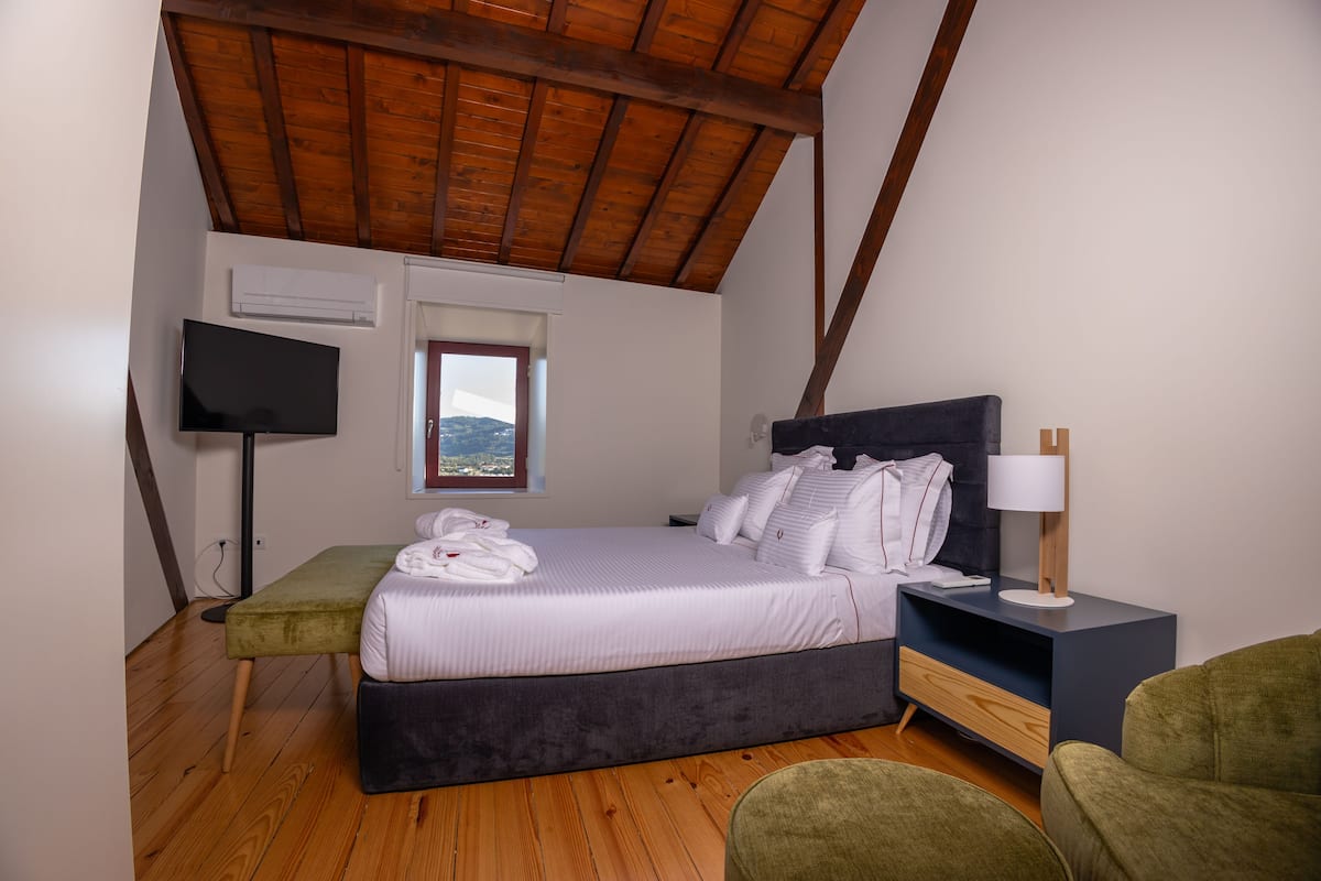 Quarto com cama, mesa de cabeceira, abajur e televisão.