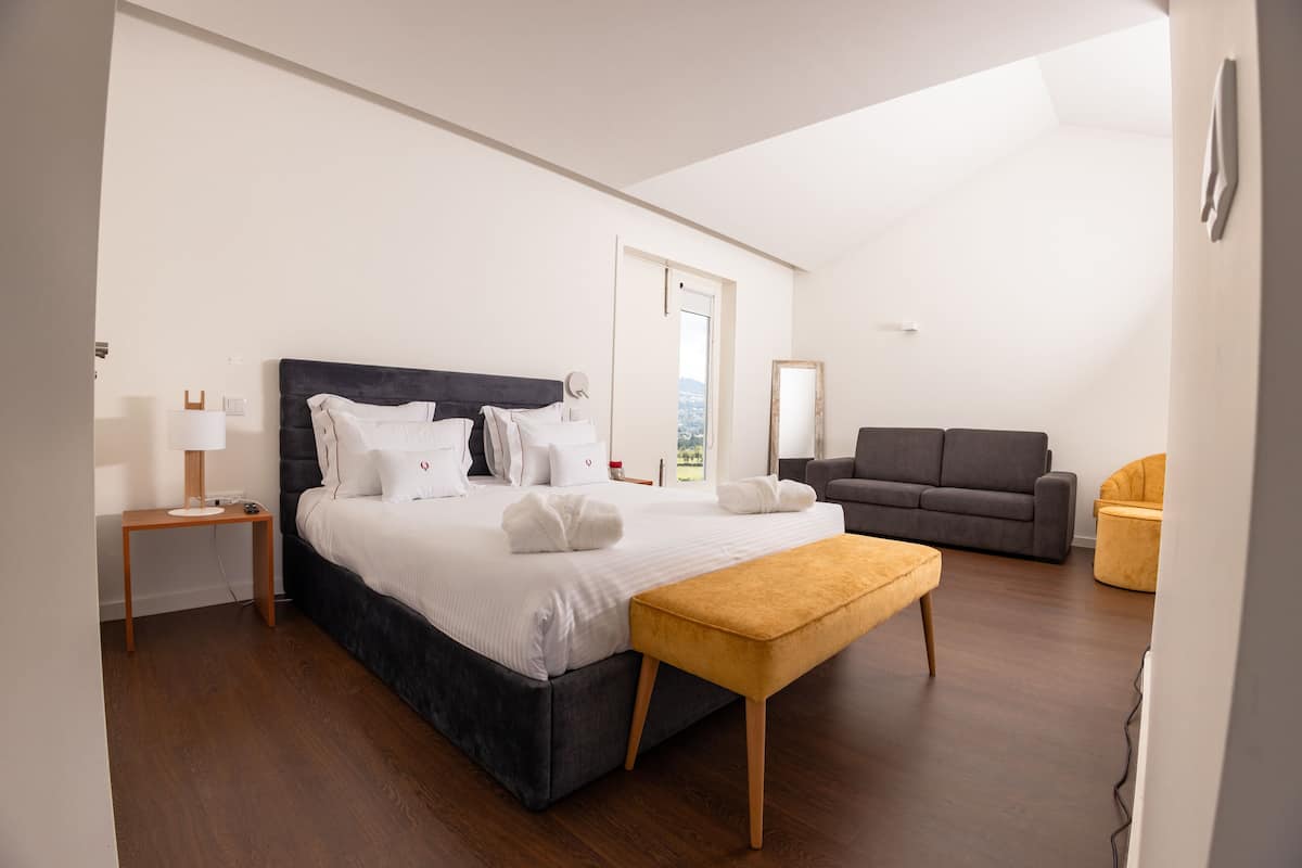Quarto moderno com uma cama grande, mesa de cabeceira, sofá e um banquinho.