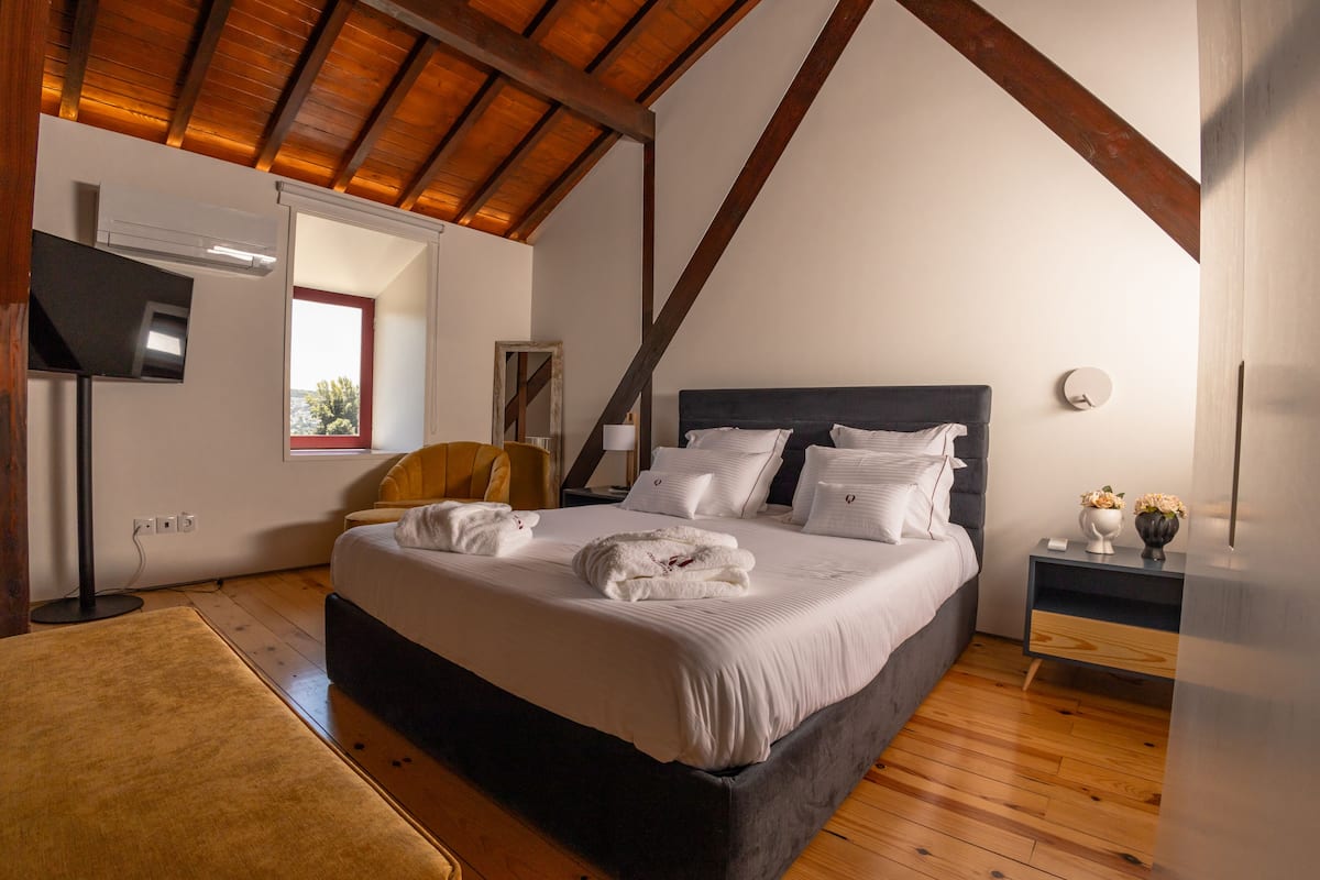 Quarto com cama grande, mesa de cabeceira, cadeira e teto de madeira.