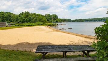 A sandy beach with a wooden picnic table and a lake in the background.