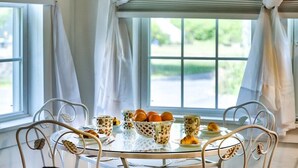 A table set with floral-patterned cups, a basket of oranges, and croissants, with white chairs around it.