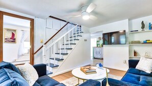 A modern living room with a blue sofa set, a round coffee table, and a staircase with a wooden railing.