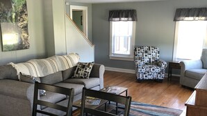 Un salon comprenant un canapé, un fauteuil à motifs, une table à manger avec des chaises et un escalier.