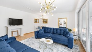 Un salon moderne avec un canapé bleu, un téléviseur à écran plat, une cheminée et un lustre.