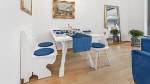 Un coin repas avec des chaises blanches et une table dressée pour quatre personnes, des coussins bleus et un lustre.