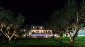 A two-story house with a well-lit front porch and a swimming pool in the background.