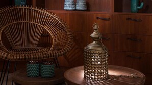 A cozy room with a wicker chair, a small round table with a lantern, and a shelf with candles and decorative items.