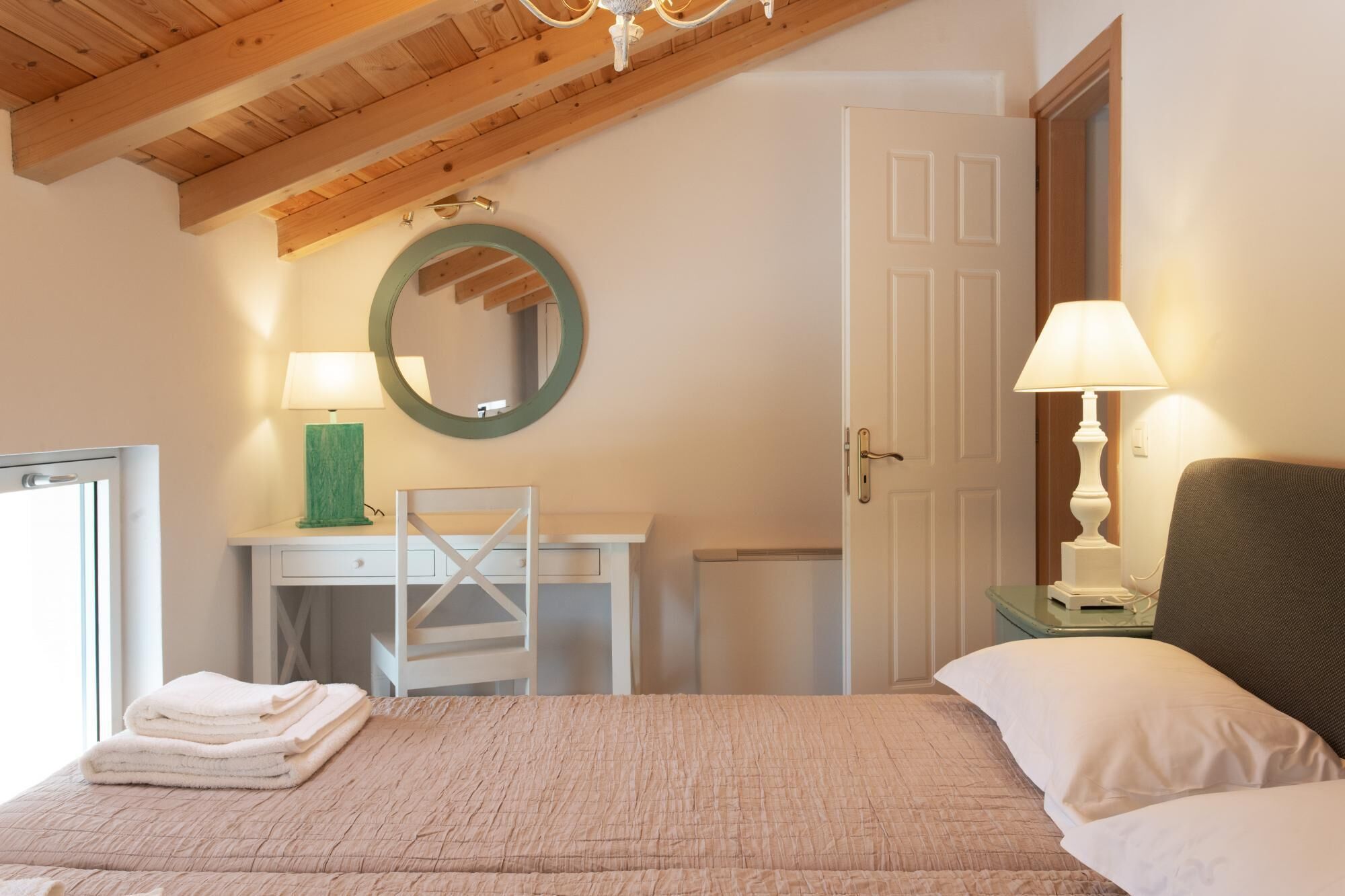 A bedroom with a bed, a desk, a chair, a mirror, and a door.