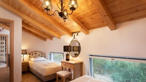 A bedroom with two beds, a wooden ceiling, a desk with a mirror, and a window with a view of greenery. - Aneli Villas - Villa Alexandra (Zakynthos)