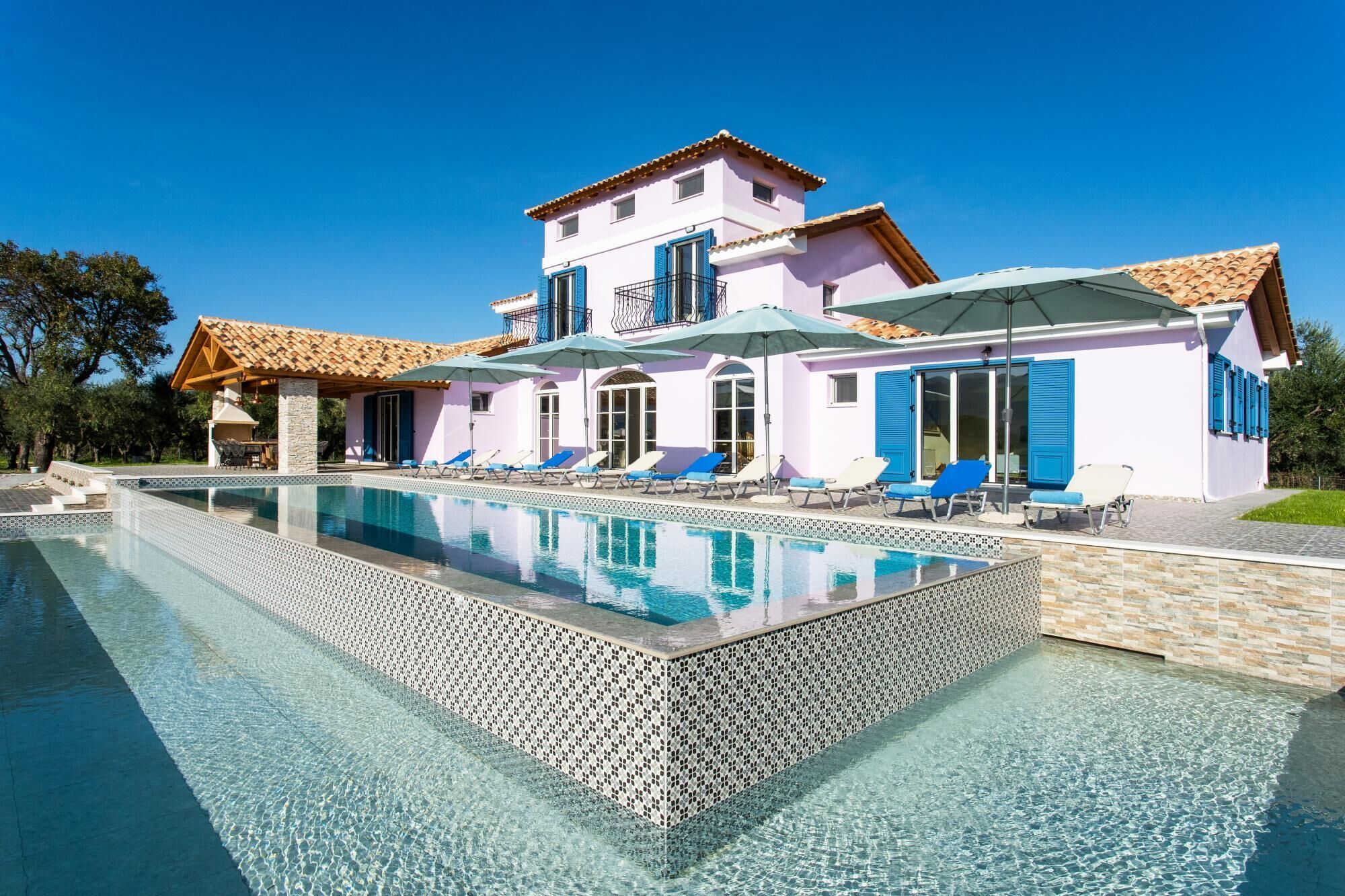 A two-story building with a swimming pool, a covered patio area, and a dining setup.