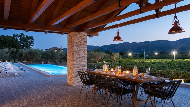 An outdoor dining area with a pool, wooden pergola, and mountain views. - Aneli Villas - Villa Alexandra (Zakynthos)