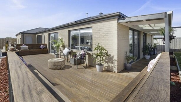 A modern house with a wooden deck, outdoor seating, and potted plants.